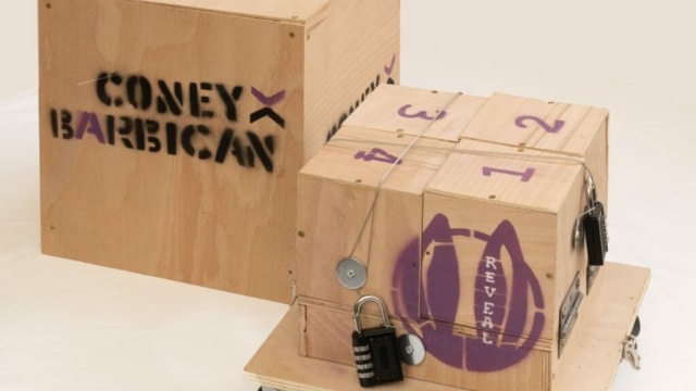 Photograph of a wooden box on wheels with letters and images spray painted onto it.