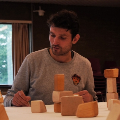 Photograph of a man drawing on a large piece of paper with wooden blocks in front of him.