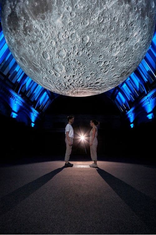 Photograph of two people standing face to face underneath a large moon.