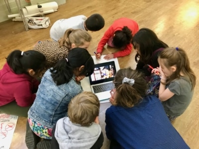 Photograph of a group of children grounded round a laptop on the floor.