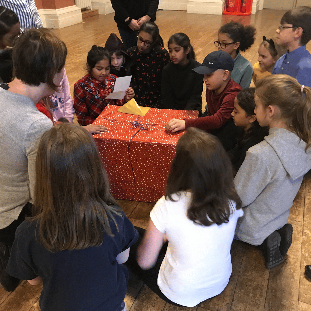 Photograph of children crowded round a large red gift wrapped box.
