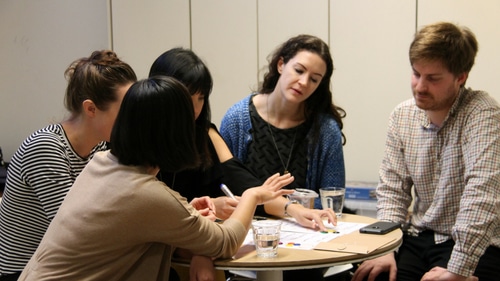 Photograph of a group of people playing a board game over a small table.